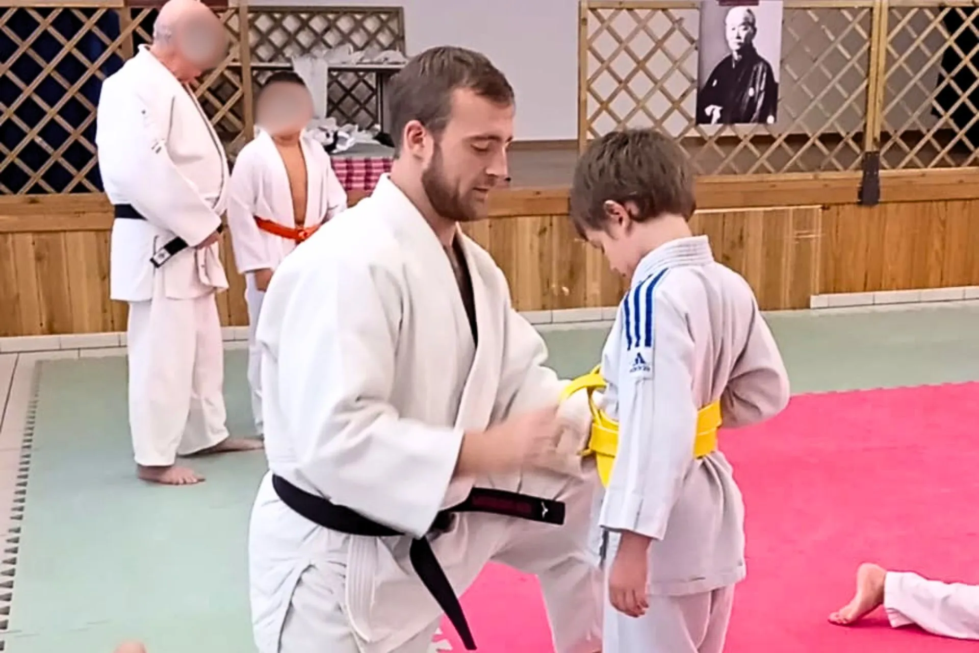 Maestro che allaccia la cintura a un bambino durante la lezione di judo